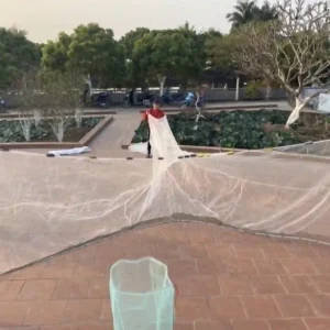 Một người đang trải tấm lưới vây cá màu trắng siêu bền trên sân gạch.