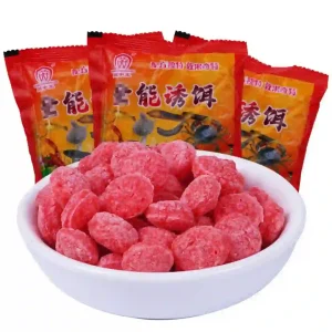 Một bát mồi viên màu đỏ dùng để bẫy tôm, cua, cá, lươn, phía sau là các gói bao bì sản phẩm.