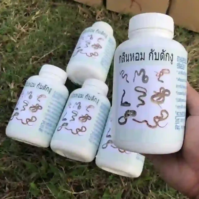 Một tay đang cầm lọ thuốc đuổi rắn dạng bột, phía sau là nhiều lọ khác trên bãi cỏ.