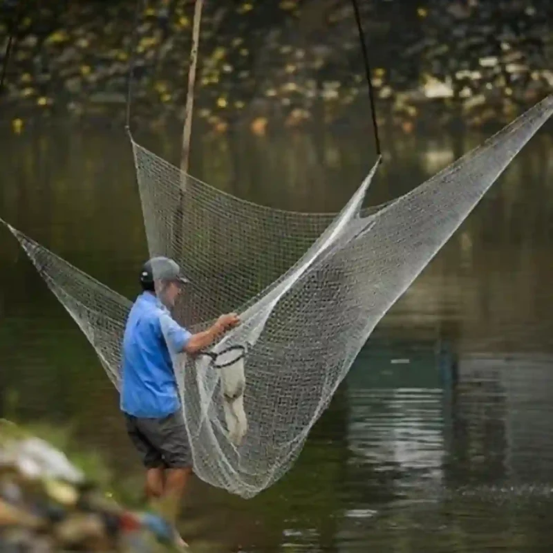 Một người đang chuẩn bị hoặc thu vó kéo cá bên bờ sông, cho thấy kích thước lớn và tính thực tiễn của sản phẩm.